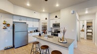 This well-appointed single-floor residence offers a thoughtfully designed open-concept layout that seamlessly connects the kitchen, dining, and living areas. The kitchen is a standout feature, boasting white shaker cabinetry, quartz countertops, a classic subway tile backsplash, stainless steel appliances — including a refrigerator, range, and microwave — and a large peninsula with bar seating, illuminated by sleek pendant lighting. Light wood-style flooring flows throughout the main living areas, enhancing the bright, airy atmosphere.

The open living room is bathed in natural light from a set of French doors leading to the outdoors, and is equipped with a ceiling fan for added comfort. Two well-sized bedrooms each feature ceiling fans, large windows with ample natural light, and plush carpeting. The full bathroom includes white cabinetry with quartz countertops, a tub-shower combination, and direct access to a walk-in closet. A dedicated in-unit laundry room provides a full-size side-by-side washer and dryer with overhead shelving. The overall aesthetic is clean and contemporary, with a neutral color palette that creates a warm and inviting atmosphere throughout.