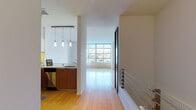 This contemporary two-floor residence showcases a thoughtfully designed open-concept layout with clean lines and modern finishes throughout. The main level features warm hardwood flooring that flows seamlessly from the kitchen through to the living area, which is bathed in natural light from expansive floor-to-ceiling windows offering urban views. A sleek staircase with chrome railings connects the two floors.

The kitchen is well-appointed with rich wood cabinetry, crisp white upper cabinets, a stainless steel backsplash, and a full suite of stainless steel appliances including a gas range with microwave above. Elegant pendant lighting hangs overhead, adding warmth to the space. A convenient powder room on the main level features a vessel sink on a dark floating vanity, adding a touch of sophistication.

The upper level houses carpeted bedrooms, each bright and airy with large windows that allow generous natural light and city views. The full bathroom features contemporary tile work, a floating vanity with integrated sink, and a curtained shower. An additional carpeted room provides flexible space for various uses. Throughout, the residence balances modern urban design with a functional, comfortable layout ideal for everyday living.