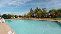 Located at 16323 Chatman Dr. in Strongsville, Ohio, this single-level community facility is centered around a standout outdoor swimming pool that serves as the focal point of the property. The pool is generously sized, featuring crystal-clear blue water and a wide surrounding deck outfitted with numerous lounge chairs, providing ample space for relaxation and recreation. The expansive sundeck allows for comfortable social gathering and sunbathing throughout the warmer months. Mature deciduous trees frame the perimeter of the pool area, offering a natural backdrop that provides both shade and a sense of privacy. The open-sky setting allows for abundant natural light throughout the day, enhancing the overall outdoor experience. The surrounding landscape is well-maintained, with green grounds visible beyond the fenced boundary of the pool area, contributing to a pleasant and inviting atmosphere. The facility is designed with community use in mind, prioritizing open, accessible outdoor space. This property offers a welcoming environment ideal for seasonal outdoor activities, with its combination of practical amenities and natural surroundings making it a functional and enjoyable community asset in the Strongsville area.