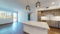 Located at 1333 N Santa Fe Ave in Vista, California, this contemporary single-floor unit showcases a thoughtfully designed open layout with modern finishes throughout. The kitchen is a standout feature, equipped with stainless steel appliances including a refrigerator, gas range, microwave, and dishwasher. Warm wood-toned cabinetry extends from floor to ceiling, complemented by white quartz countertops and a classic subway tile backsplash. A large kitchen island with a striking quartz waterfall countertop anchors the space, illuminated by a pair of stylish smoked-glass pendant lights. The open-concept living area flows seamlessly from the kitchen and offers access to an outdoor space through sliding glass doors, filling the room with natural light. Wood-look plank flooring runs throughout the main living and kitchen areas, while plush carpet provides comfort in the bedrooms. Each bedroom benefits from natural light via large windows with outdoor views, and ceiling fans add to the comfort. The bathrooms are finished with wood-toned vanities, quartz countertops, undermount sinks, large mirrors, and tub-shower combinations with clean white tile surrounds. A carpeted hallway connects the private areas of the unit, completing this well-appointed, modern living space.