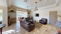 Located on Caminito Cantilena in San Diego's 92128 zip code, this single-story space features an open, flowing layout finished with large-format travertine tile flooring throughout. Natural light fills the interior through generous windows, with views of a sparkling outdoor pool and surrounding landscaping visible from the main living and dining areas.

The spacious living room anchors the space, centered around a handsome raised-hearth fireplace with a stone surround and decorative mantle. Recessed lighting and two Tiffany-style pendant fixtures illuminate the room, complementing the warm, neutral color palette. The open layout connects seamlessly to a casual dining nook, which benefits from an abundance of natural light streaming through a large window bank overlooking the pool area. A decorative pendant light fixture adds character to the dining space.

A welcoming entry foyer features a glass-panel door, allowing additional natural light to filter in, along with an interior pass-through window that connects to the main hall. Throughout the space, architectural details such as recessed ceilings, defined beam lines, and built-in shelving niches add visual interest. The overall ambiance is bright, comfortable, and well-suited for communal gathering.