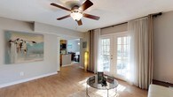 Tally Square is a thoughtfully designed single-floor residence that offers a comfortable and functional layout throughout. The living area serves as the heart of the home, featuring warm hardwood-style flooring, a ceiling fan with light fixture, and a set of elegant French doors framed by sheer floor-to-ceiling drapes that flood the room with natural light and provide access to the outdoors. The space flows seamlessly into a dedicated dining area, complete with its own window dressed in sheer curtains, creating a bright and inviting atmosphere for meals. The kitchen is equipped with wood-tone cabinetry, dark stone-look countertops, and essential appliances, connecting conveniently to the main living areas via a louvered door passageway. The primary bedroom is a serene retreat with plush carpeting, ample space, and direct access to a generously sized walk-in closet outfitted with extensive shelving and hanging rods. The primary bathroom features warm wood vanity cabinetry, stone-look countertops, and abundant overhead storage. Additional bedrooms are carpeted and well-sized, each with their own closet space. A versatile flex room with hardwood-style flooring offers potential as a home office or study. Neutral gray tones throughout the residence create a cohesive and modern aesthetic.