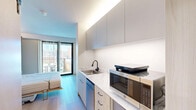 Located on the sixth floor at 145 Leavenworth Street in San Francisco's civic center neighborhood, this efficiently designed studio maximizes every square foot through smart architectural choices and modern finishes throughout.

The main living area centers around a built-in Murphy bed flanked by integrated open shelving and storage, allowing the space to function flexibly. Warm ambient lighting runs along the ceiling's upper edge, complementing the light wood tones used throughout. A full-height sliding glass door floods the room with natural light and frames views of the surrounding cityscape, with adjustable vertical blinds for privacy.

The galley-style kitchenette is outfitted with sleek upper cabinetry in a soft gray finish, a marble-look countertop, a single-basin sink with a matte black faucet, a microwave, and a dishwasher — all the essentials compactly arranged. Light hardwood flooring runs continuously through the living and kitchen areas, lending warmth and cohesion to the open layout.

A sliding barn-style door with frosted glass panels leads to a closet, while a separate entry door features a modern wood veneer finish. The bathroom is clean and minimalist, finished in large-format white tile, and includes a wall-mounted sink, toilet, a walk-in roll-in shower with matte black grab bars, and a movable wood storage bench — reflecting an accessible and thoughtfully inclusive design.