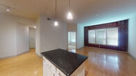 This single-floor residence offers a thoughtfully designed open-concept layout that seamlessly connects the kitchen, dining, and living areas. The kitchen is a standout feature, equipped with stainless steel appliances, white cabinetry with a lattice wine rack detail, a dark granite countertop, a tile backsplash, and a central island with pendant lighting overhead. The warm hardwood flooring extends throughout the main living areas, complemented by soaring ceilings that enhance the sense of openness. A charming exposed brick accent wall in the living area adds an industrial yet inviting character to the space, while multiple windows fitted with blinds allow ample natural light to filter in. The bedroom is generously sized, featuring plush carpeting, a ceiling fan, and large windows that brighten the room. It includes a spacious walk-in closet outfitted with wire shelving on multiple walls, providing excellent storage capacity. The bathroom is clean and functional, featuring a soaking tub with a tiled shower surround and chrome fixtures. Throughout the residence, neutral tones and consistent finishes create a cohesive, move-in-ready environment suited for comfortable everyday living.