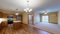 Located at 101 12th Ave S in Sartell, Minnesota, this single-floor unit offers a well-designed, functional layout with a warm, neutral color palette throughout. The open-concept kitchen is a standout feature, outfitted with rich wood cabinetry, light countertops, a stainless steel refrigerator, electric range, built-in microwave, and dishwasher. A central island provides additional prep and storage space, while hardwood-style flooring adds a classic, durable finish to the kitchen and entryway areas. The dining area is illuminated by an elegant chandelier, creating a welcoming atmosphere that flows naturally into the spacious living room. The living room is finished with plush carpeting, a ceiling fan, and a sliding glass door that opens to a private balcony, allowing natural light to fill the space. Two well-proportioned bedrooms each feature ceiling fans, carpet flooring, baseboard heating, and windows that bring in outside views. The bathroom is cleanly appointed with a wood-framed vanity mirror, single-sink vanity, and a full tub-shower combination with tile flooring. A dedicated in-unit laundry room with wire shelving and full-size washer and dryer hookups adds everyday convenience. Baseboard heating is present throughout, ensuring comfort during Minnesota winters.
