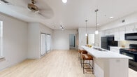 This single-floor residence at 11925 Jones Rd in Houston, Texas offers a thoughtfully designed layout that balances comfort and modern style. The open-concept living and kitchen area is bright and airy, featuring light hardwood-style flooring, a ceiling fan, track lighting, and a set of French doors that invite natural light into the space. A large window further enhances the room's welcoming atmosphere.

The kitchen is a standout feature, equipped with crisp white cabinetry, white quartz countertops, and a large island with a double-basin sink and bar seating for casual dining. Black appliances — including a refrigerator, electric range, and over-the-range microwave — provide a sleek contrast to the bright cabinetry. Pendant lighting above the island adds a refined touch.

The bedrooms are carpeted for comfort, each outfitted with a ceiling fan and window with blinds. The primary bedroom includes access to a generously sized walk-in closet with built-in shelving and dual hanging rods, providing ample storage.

The bathroom features warm earth-toned tile surrounding a full soaking tub and shower combination, complemented by light wood-style flooring and a white vanity. The neutral color palette and clean finishes carry throughout the entire space, creating a cohesive and move-in-ready environment.