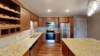 This single-floor residence offers a thoughtfully designed layout with a cohesive blend of warm tones and modern finishes throughout. The kitchen serves as a standout feature, showcasing rich medium-toned wood cabinetry with shaker-style doors, speckled granite countertops, and a full suite of stainless steel appliances including a range, built-in microwave, refrigerator, and dishwasher. Recessed lighting illuminates the space, while a central island with matching granite provides additional prep and seating space. Hardwood-style flooring flows through the kitchen and into the adjoining areas, creating a seamless transition.

The living area is anchored by a striking stone-surround fireplace, adding warmth and visual interest to the room. Plush carpeting defines the living and bedroom spaces, offering a comfortable contrast to the hard flooring elsewhere. The bedroom features a window overlooking a balcony and the surrounding neighborhood, with baseboard heating providing practical comfort.

The bathroom is finished with the same granite countertop found throughout, paired with a rich wood vanity, an undermount sink, and a well-lit vanity mirror. A grab bar adds a functional accessibility element. Neutral wall tones throughout the unit create a calm, welcoming ambiance.
