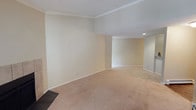 This single-floor space offers a clean, open layout designed for versatile living. The main living area is finished with wall-to-wall beige carpeting that lends warmth underfoot and complements the soft, neutral cream-toned walls throughout. Crown molding lines the ceiling perimeter, adding a refined architectural detail that elevates the overall finish of the space. The ceiling features a textured surface, contributing subtle visual interest while maintaining a classic aesthetic. The layout flows naturally from the primary living area into an adjacent secondary space, connected by an open archway transition that creates a sense of depth and continuity. Recessed lighting in the secondary area provides focused, ambient illumination, enhancing the welcoming atmosphere. White baseboard trim frames the flooring throughout, offering a crisp contrast to the warm wall tones. The space is bright and airy, benefiting from an even, diffused light quality that makes the interiors feel open and inviting. Overall, the space presents a well-maintained, move-in ready environment with timeless finishes and a cohesive design sensibility suited to a variety of functional arrangements.