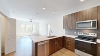 Located at 12890 S Black Bob Rd in Olathe, Kansas, this well-appointed single-floor residence offers three bedrooms and one bathroom with a thoughtfully designed open-concept layout. The kitchen is a standout feature, showcasing rich walnut-toned cabinetry, quartz countertops with subtle marble veining, a grey tile backsplash, and a full suite of stainless steel appliances including a range, microwave, dishwasher, and French door refrigerator. A peninsula with an integrated sink provides both additional prep space and a natural connection to the living area. The living room is bright and airy, with light hardwood flooring, a ceiling fan, and large windows and a glass door that invite abundant natural light and outdoor views of the surrounding greenery. The bedrooms feature plush carpeting, ceiling fans, and generous windows with nature views; the primary bedroom includes a dedicated closet with built-in shelving. The bathroom mirrors the home's modern aesthetic with a walnut vanity, quartz countertop, a large framed mirror, and a tiled walk-in shower. Additional conveniences include an in-unit washer and dryer. The space is finished with clean white walls and consistent modern hardware throughout, creating a cohesive, contemporary feel.