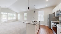 Located at 5654 Orange Summit Dr. in Lewis Center, Ohio, this well-appointed 3-bedroom, 2-bathroom single-story home offers a thoughtfully designed layout filled with natural light. The open-concept living and kitchen area serves as the heart of the home, anchored by a central island with striking granite countertops, an undermount sink, and stylish pendant lighting. White shaker cabinetry pairs with stainless steel appliances, including a refrigerator, range, and microwave. Vaulted ceilings in the living area create an airy, expansive feel, while multiple windows frame outdoor views and flood the space with daylight. Warm hardwood-style flooring runs through the main living and kitchen areas, transitioning to plush carpeting in the bedrooms. The generously sized primary bedroom includes its own access to a balcony. Additional bedrooms feature ceiling fans, neutral tones, and ample natural light. Bathrooms are finished with granite-topped vanities and gold hardware accents. A dedicated laundry room with full-size washer and dryer hookups adds everyday convenience. With seven closets throughout, storage is abundant. The home's clean, neutral palette and modern finishes create a bright and welcoming atmosphere throughout.