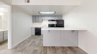 Located at 3515 E Bell Rd in Phoenix, AZ, this efficient single-story unit offers a well-designed layout across a compact footprint. Wood-look plank flooring runs consistently throughout the space, providing a cohesive and easy-to-maintain aesthetic.

The kitchen serves as a functional centerpiece, featuring gray flat-front cabinetry, light stone-finish countertops, and a peninsula with bar seating that defines the space. Black appliances — including a range, refrigerator, and dishwasher — are included. An overhead skylight panel brings additional brightness to the kitchen area.

The bedroom is a comfortable, well-proportioned room with a window allowing natural light and direct access to a dedicated walk-in closet equipped with built-in shelving, offering practical storage. The textured ceiling adds a subtle architectural detail to the room.

The bathroom is clean and straightforward, featuring a single-sink vanity with a light countertop, a full tub/shower combination with a white surround, and wood-look tile flooring that ties in with the rest of the unit. The overall design is neutral and modern, making the space easy to personalize.