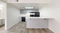 Located at 3515 E Bell Rd in Phoenix, AZ, this efficient single-story unit offers a well-designed layout across a compact footprint. Wood-look plank flooring runs consistently throughout the space, providing a cohesive and easy-to-maintain aesthetic.

The kitchen serves as a functional centerpiece, featuring gray flat-front cabinetry, light stone-finish countertops, and a peninsula with bar seating that defines the space. Black appliances — including a range, refrigerator, and dishwasher — are included. An overhead skylight panel brings additional brightness to the kitchen area.

The bedroom is a comfortable, well-proportioned room with a window allowing natural light and direct access to a dedicated walk-in closet equipped with built-in shelving, offering practical storage. The textured ceiling adds a subtle architectural detail to the room.

The bathroom is clean and straightforward, featuring a single-sink vanity with a light countertop, a full tub/shower combination with a white surround, and wood-look tile flooring that ties in with the rest of the unit. The overall design is neutral and modern, making the space easy to personalize.