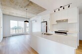 This contemporary apartment in Montréal's Savane district presents a harmonious blend of modern design and functional living. The 57-square-meter space is efficiently laid out across a single floor, featuring two bedrooms, including a primary bedroom of 10 square meters. The open-concept living area is a highlight, showcasing a stylish kitchen with a central island, stainless steel appliances, and ample counter space. The space is bathed in natural light, courtesy of large windows that offer urban views and create a bright, airy atmosphere.

The bathroom is a study in minimalist elegance, with a floating vanity, large mirror, and a glass-enclosed shower over a sleek bathtub. Throughout the apartment, warm wood flooring contrasts beautifully with crisp white walls, while exposed concrete ceilings add an industrial chic touch. The bedrooms continue the theme of simplicity and light, with one room featuring a striking floor-to-ceiling window. Storage solutions are seamlessly integrated, including a dedicated closet space. This apartment at 4986 Pl De La Savane embodies modern urban living, offering a perfect balance of style, comfort, and functionality in the heart of Montréal.