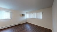 This 1-bedroom, 1-bathroom unit is thoughtfully laid out across a single floor, offering a clean and functional living environment. Rich, dark hardwood-style flooring flows consistently throughout the main living areas, creating a cohesive and warm aesthetic.

The spacious living area is bright and airy, with large windows dressed in vertical blinds that allow generous natural light to fill the room. A wall-mounted air conditioning unit and baseboard heating provide year-round climate control, while a ceiling fan adds additional comfort and airflow.

The kitchen is a standout feature, finished with crisp white shaker-style cabinetry, light countertops, and a full suite of stainless steel appliances including a refrigerator, dishwasher, and range. Under-cabinet lighting adds both functionality and ambiance to the well-organized cooking space.

The bedroom is comfortably sized with two windows, a ceiling fan, and a reach-in closet offering practical storage. Hardwood-style flooring continues seamlessly into this room.

The bathroom is clean and well-appointed, featuring a tiled shower-tub combination, a white vanity with ample drawer storage, brushed nickel hardware, and matching hardwood-style flooring that ties the space together cohesively.