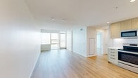 Located at 1150 E Street in San Diego's vibrant East Village neighborhood, this modern one-bedroom, one-bathroom residence offers a thoughtfully designed open-concept layout finished with light hardwood flooring throughout. The combined living, dining, and kitchen area forms the heart of the home, bathed in natural light from floor-to-ceiling windows and a sliding glass door that opens to a private balcony with sweeping city views. The contemporary kitchen is well-appointed with light wood cabinetry extending to the ceiling, white subway tile backsplash, quartz countertops, and a full suite of stainless steel appliances including a range, microwave, dishwasher, and refrigerator. The bedroom is a bright, comfortable retreat featuring large windows and balcony access that frame open outdoor views. The full bathroom is finished with marble-style tiled walls surrounding a soaking tub and shower combination, a wood-toned vanity with an undermount sink, and a large mirror. Additional conveniences include in-unit laundry and a closet. Clean white walls and consistent light-toned flooring unify the space, creating a bright and modern aesthetic throughout.