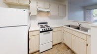 This single-floor unit is designed with a straightforward, functional layout that makes efficient use of its space. The open-concept kitchen flows directly into the living area, separated by a half-wall peninsula that provides additional counter space and a casual dining or prep surface. The kitchen is equipped with light wood cabinetry offering ample storage, white appliances including an electric range and refrigerator, a stainless steel sink, and tile flooring that extends throughout the cooking area. Light-colored countertops keep the space feeling bright and clean.

The living area transitions to plush wall-to-wall carpeting, creating a comfortable, cohesive feel. Neutral white walls throughout lend a clean, versatile backdrop. A window along the far wall allows natural light to filter into the space.

The bedroom is a well-proportioned room with the same warm carpeting, white walls, and a window with blinds that overlooks a greenery-filled outdoor area, bringing in natural light and pleasant views.

The bathroom is finished with tile flooring, a full soaking tub and shower combination, a vanity with under-sink cabinet storage, a large mirror, and bright overhead lighting, maintaining the unit's clean, neutral aesthetic.