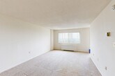 Located at 2445 Lyttonsville Rd in Silver Spring, MD, this efficiently designed unit offers a thoughtful layout across a single floor. The main living area is bright and open, featuring neutral wall-to-wall carpeting, crisp white walls, and a large window dressed with vertical blinds that invites natural light into the space. A radiator beneath the window provides reliable heating, contributing to a clean, uncluttered aesthetic. The kitchen is positioned adjacent to the living area and features warm wood cabinetry with granite-style countertops, offering functional workspace and storage. The unit includes two bathrooms: one full bathroom complete with a tiled tub-surround accented by mosaic tile detailing, a toilet, tile flooring, and a wood vanity with a white countertop; the second bathroom features a matching wood vanity with a recessed medicine cabinet mirror, providing additional convenience. A dedicated walk-in closet with dual hanging rods and carpeted flooring offers generous storage capacity. The entry door opens directly into the main living space, creating a straightforward and accessible flow throughout. Overall, the unit presents a clean, neutral palette with practical finishes suited for comfortable everyday living.