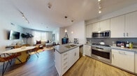 This well-appointed single-floor residence offers a thoughtfully designed open-concept layout that seamlessly connects the kitchen, dining, and living areas. The kitchen is a functional centerpiece, featuring white flat-front cabinetry, granite countertops, a gray subway tile backsplash, and a full suite of stainless steel appliances including a gas range, built-in microwave, dishwasher, and refrigerator. A peninsula with an undermount sink and pendant lighting above provides additional prep space and casual seating. Wood-look flooring flows throughout the main living area, which is bright and welcoming with natural light from multiple windows. The living room offers comfortable proportions with outdoor views framed by sheer curtains and horizontal blinds. Two bedrooms provide restful retreats, each with generous natural light and neutral carpet or hardwood-style flooring. The primary bedroom features a four-poster bed frame and views to the outdoors. Both bathrooms are finished with granite-topped vanities, wood-look tile flooring, and glass-enclosed walk-in showers with clean tile surrounds. The overall aesthetic is modern and cohesive, with a neutral palette and quality finishes that create a polished, livable environment.