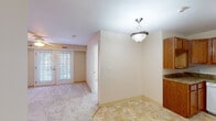 This single-floor unit offers a practical and well-organized layout designed for comfortable everyday living. The open-concept design connects the kitchen directly to the living area, creating a cohesive and functional shared space. The kitchen is equipped with warm oak cabinetry extending to the ceiling for ample storage, granite-style countertops, and white appliances including a range, dishwasher, and refrigerator. Tile flooring runs throughout the kitchen and dining area, transitioning to plush carpet in the living and bedroom spaces.

The living area receives natural light through a glass-paneled exterior door, contributing to a bright and welcoming atmosphere. A pendant light fixture illuminates the dining nook adjacent to the kitchen, where additional cabinetry provides further storage convenience.

Two carpeted bedrooms offer comfortable retreats, with one featuring dual windows that bring in generous natural light. The full bathroom includes a wood-toned vanity with a white countertop, a wall mirror, and tile flooring consistent with the rest of the unit. Throughout the space, cream-toned walls and yellow-accented baseboards reinforce a clean, neutral aesthetic.