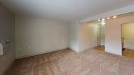 Located at 2335 Springbrook Pkwy SE in Grand Rapids, Michigan, this single-floor unit offers a cohesive, functional layout designed for comfortable everyday living. A consistent design language runs throughout the space, highlighted by white beadboard wainscoting that lines the walls of the main living areas, adding a clean, classic architectural detail.

The living areas feature warm, neutral-toned carpet and are bathed in natural light through multiple windows fitted with horizontal blinds. One carpeted room includes a ceiling fan with a built-in light fixture and a window overlooking greenery outside. An adjacent carpeted space features vertical blinds alongside a wide window, providing flexibility for use as a living or dining area. An entry area with hard flooring connects the main rooms and leads to a white entry door.

The kitchen is efficiently arranged in a galley configuration, featuring warm oak cabinetry, granite countertops, a stainless steel sink, a gas range, and a refrigerator. An in-unit washer and dryer are integrated directly into the kitchen area, adding everyday convenience.

The bathroom is well-appointed with oak cabinetry, granite countertops, a framed mirror, a vanity light fixture, tile flooring, and a full tub and shower combination with grab bars installed for added accessibility.