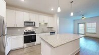 Located in St. Augustine, FL, this single-story, 3-bedroom, 2-bathroom home offers a thoughtfully designed open-concept layout. The kitchen is a standout feature, showcasing white shaker cabinetry, granite countertops, a classic subway tile backsplash, and a full suite of stainless steel appliances including a refrigerator, range, and microwave. A central island with pendant lighting above provides additional prep space and connects seamlessly to the living area, which features wood-look flooring and a ceiling fan. The spacious primary bedroom includes plush carpeting, a ceiling fan, and natural light from a large window. The additional bedrooms are similarly appointed with carpet and ceiling fans, offering comfortable, versatile spaces. Both bathrooms are finished with granite-topped vanities and wood-look flooring; the primary bath includes a glass-enclosed walk-in shower. A dedicated laundry room houses a full-size washer and dryer. Three closets provide ample storage throughout. The home's clean, neutral palette and modern finishes create a bright, cohesive ambiance throughout every room.