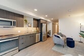 Located at 1410 NE 65th St in Seattle's vibrant Bryant neighborhood, this one-bedroom, one-bathroom unit offers a well-designed, single-level layout that maximizes every square foot of living space. The open-plan living, dining, and kitchen area forms the heart of the unit, featuring light wood-look flooring, recessed lighting, and a clean, contemporary aesthetic throughout. The kitchen is fully equipped with stainless steel appliances — including a range, microwave, dishwasher, and refrigerator — complemented by dark wood-grain cabinetry that extends to the ceiling for ample storage, and a neutral tile backsplash. A hallway connects the main living area to the private bedroom, which includes a sliding door closet and soft, neutral tones that create a calm retreat. An additional closet provides further storage convenience. The combined bathroom and laundry space features a glass-enclosed walk-in shower with large-format white tile and polished chrome fixtures. Thoughtful details such as a floating wall shelf in the hallway and a compact yet functional layout make this unit an efficient and modern living space well-suited for Seattle urban living.