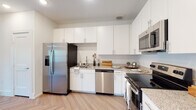 This well-designed single-floor residence offers a clean, contemporary aesthetic throughout. The kitchen is a standout feature, outfitted with crisp white cabinetry extending to the ceiling, granite-look countertops, and a full suite of stainless steel appliances including a side-by-side refrigerator with ice and water dispenser, a dishwasher, an electric range, and an over-the-range microwave. The kitchen flows seamlessly into the main living area, which is distinguished by a striking herringbone-patterned luxury vinyl plank floor that adds warmth and visual interest to the open layout. Natural light filters in through multiple windows, enhancing the bright, airy atmosphere of the living space. The bedroom is generously sized, featuring a ceiling fan, light wood-tone flooring, and access to a spacious walk-in closet with wire shelving on multiple walls for ample organization. The bathroom is thoughtfully appointed with white subway tile surrounding the soaking tub and shower, a granite-topped vanity with white cabinetry, and wood-tone flooring that ties the space together. Throughout the residence, consistent light tones, clean lines, and modern finishes create a cohesive and inviting living environment.