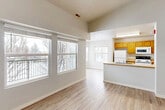 This 2-bedroom, 1-bathroom residence is thoughtfully organized across a single floor, offering a functional and comfortable living environment. The open-concept living and dining area is a standout feature, boasting soaring vaulted ceilings that amplify the sense of space. Large windows with horizontal blinds line the living area, inviting generous natural light and offering views of surrounding trees and the outdoors. Light-toned hardwood-style flooring runs consistently throughout the home, lending a clean, cohesive aesthetic.

The kitchen is positioned adjacent to the living and dining spaces, defined by a peninsula counter that provides a natural division while maintaining an open feel. Warm honey-toned wood cabinetry, light countertops, a double-basin sink, and white appliances — including a refrigerator, electric range, and microwave — equip the kitchen for everyday use.

The primary bedroom is generously sized, featuring vaulted ceilings and a large window with balcony access. The second bedroom is bright and well-proportioned, with multiple windows offering outdoor views. The hallway connects the bedrooms to the full bathroom, which includes a single-sink vanity with wood cabinetry, a tub-shower combo, and hardwood-style flooring. A separate hallway entry area provides convenient access to the unit's front door and an in-unit closet.