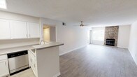This single-floor residence offers a clean, functional layout designed for comfortable everyday living. The open-concept main area seamlessly connects the kitchen and living room, with light-toned wood-look flooring running throughout. The living room is highlighted by a floor-to-ceiling stone fireplace, a ceiling fan, and a large window that invites natural light and outdoor views. The kitchen features white shaker-style cabinetry with brushed nickel hardware, a peninsula with an integrated sink, light countertops, and stainless steel appliances including a dishwasher. A textured ceiling adds character throughout the common areas. The bedrooms are finished with plush wall-to-wall carpeting and offer generous proportions, with windows providing natural light. The bathroom is outfitted with a full tub-shower combination, a toilet, and a vanity with chrome fixtures and clean white finishes. A dedicated in-unit laundry closet houses a full-size top-loading washer and dryer with an overhead storage shelf, adding everyday convenience. Throughout the space, neutral tones, white trim, and consistent finishes create a cohesive and inviting atmosphere well-suited for a range of lifestyles.