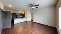 This single-floor unit presents a cohesive, modern design highlighted by rich hardwood-style flooring throughout the main living areas and plush carpet in the bedrooms. The open-concept living and kitchen space is anchored by a peninsula with granite countertops and an undermount sink, complemented by pendant lighting in a warm yellow tone. Dark espresso cabinetry lines the kitchen walls, paired with a tile backsplash, black appliances including a gas range and built-in microwave, and track lighting overhead. A ceiling fan with an integrated light fixture serves the living area, which connects seamlessly to additional rooms via a central hallway.

The bedrooms are well-proportioned, each equipped with a ceiling fan and window fitted with blinds that allow natural light to filter in. At least one bedroom includes a sliding-door closet with built-in shelving. The primary bathroom features a long double-vanity with granite countertops, dark cabinetry, and a soaking tub with a shower curtain rod, with direct access to a walk-in closet. A secondary bathroom offers a single-sink vanity with matching granite, a wall-mounted cabinet, and a separate shower area with grab bars.