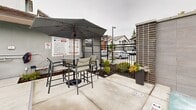 Located at 1005 E Atherton Dr in Manteca, California, this outdoor amenity space centers around a generously sized, crystal-clear swimming pool that serves as the focal point of the community. The pool area is thoughtfully designed to encourage relaxation and socializing, with a wide surrounding deck outfitted with rows of lounge chairs positioned to maximize sun exposure throughout the day. A spa is integrated into the layout, providing an additional option for leisure. Tall palm trees line portions of the pool deck, lending a resort-inspired aesthetic that complements the warm California climate. A covered patio area offers a shaded retreat with high-top seating and umbrella-shaded tables, ideal for outdoor dining or casual gatherings. Safety amenities, including life-saving equipment, are visibly posted and accessible. The space is enclosed by sleek iron fencing, providing security while maintaining open sightlines to the surrounding multi-story residential buildings. Manicured planters with flowering accents add color and greenery throughout. The overall design balances functionality with aesthetic appeal, creating a welcoming outdoor environment suited for both active recreation and quiet relaxation.