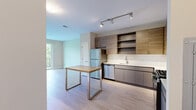 Located at 150 Glover Ave in Norwalk, CT, this thoughtfully designed one-bedroom, three-bathroom residence offers a modern aesthetic throughout its efficiently organized single-floor layout. Light hardwood-style flooring flows seamlessly through every room, complementing the neutral warm-toned walls that create a clean, cohesive atmosphere.

The open kitchen is a standout feature, showcasing two-tone cabinetry with wood-grain upper cabinets and sleek gray lower cabinets, white quartz countertops, and a full suite of stainless steel appliances including a gas range, dishwasher, refrigerator, and built-in microwave. Open shelving adds functional style, and a center dining table with a metal frame provides casual seating within the space.

The bedroom is well-proportioned, bathed in natural light from multiple windows that frame lush, tree-lined outdoor views. A dedicated closet offers convenient storage. The hallway connects the living areas to the bathrooms with ease, including a primary bath featuring a stylish blue-gray double vanity with white countertops, a glass-enclosed walk-in shower, and contemporary lighting.

A private balcony extends the living space outdoors, offering sweeping views of mature trees and open sky — a serene retreat above the treetops.