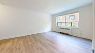 Located on Queen Street East in Toronto's Upper Beaches neighbourhood, this three-bedroom, one-bathroom unit offers a thoughtfully updated interior across a single floor. Light wood laminate flooring runs throughout, complementing the clean white walls and creating a bright, cohesive feel.

The open-concept kitchen and living area forms the heart of the unit. The kitchen is outfitted with white cabinetry, dark stone countertops, a herringbone tile backsplash, and stainless steel appliances including a French door refrigerator, dishwasher, and range. The adjoining living area is spacious and filled with natural light from a large multi-pane window, with a radiator unit positioned below.

The primary bedroom is a well-proportioned room featuring a corner window that invites greenery views and natural light. A closet with panelled doors provides dedicated storage. The two additional bedrooms are similarly bright, each with windows and light-toned walls — one featuring a radiator beneath a window framing lush ivy-covered surroundings.

The bathroom is cleanly finished with large-format grey floor tiles, white subway tile surrounding the soaker tub, and a window for natural ventilation. A hallway connects the rooms efficiently, with a dedicated closet offering additional storage. Elegant three-panel interior doors are featured throughout the unit.