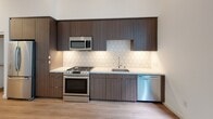 Located at 110 W Ocean Blvd in the heart of Long Beach, California, this modern single-floor residence showcases a clean, contemporary design throughout. Light wood-look flooring runs seamlessly across the open layout, complementing the crisp white walls and adding warmth to every room.

The kitchen is a standout feature, appointed with rich dark wood cabinetry that extends to the ceiling for maximum storage, a white quartz countertop, and a striking hexagonal tile backsplash. A full suite of stainless steel appliances includes a gas range, built-in microwave, dishwasher, and a French door refrigerator — all thoughtfully integrated into the cabinetry for a cohesive look.

The living area is bright and airy, benefiting from floor-to-ceiling windows that frame views of lush greenery, allowing natural light to fill the space generously. A walk-in closet provides ample storage.

The bathroom is finished with a wood-toned vanity, white quartz countertop, a large mirror, built-in shelving, and a tiled soaking tub with a sliding glass enclosure — offering both style and functionality.

Completing the unit is an in-unit stacked washer and dryer, adding everyday convenience to this well-appointed Long Beach residence.