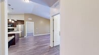 Located at 4200 N Seasons View Dr in Lehi, Utah, this 2-bedroom, 2-bathroom residence offers a well-organized, single-level layout designed for comfortable everyday living. The open-concept kitchen is a standout feature, showcasing rich dark-wood cabinetry with brushed nickel hardware, a white countertop center island, pendant lighting, black appliances, and a double stainless steel sink — all set atop wood-look plank flooring. The kitchen flows seamlessly into the living room, which is highlighted by vaulted ceilings, a ceiling fan, and a sliding glass door that invites natural light and outdoor views. The primary bedroom offers a cozy carpeted floor and generous proportions, while the second bedroom also features soft carpet and a window with exterior views. Both bedrooms are serviced by well-appointed bathrooms: one with a full tub-shower combination, white cabinetry, and tile flooring; the other with a walk-in style shower, grab bar, and wood-look tile. A hallway and dedicated closet add to the functional layout. Neutral warm-toned walls, clean white trim, and consistent finishes throughout give this residence a polished and cohesive aesthetic.