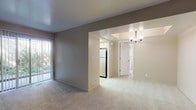 This single-floor residence offers a practical and comfortable layout designed for everyday living. The spacious living room is finished with plush wall-to-wall carpeting and neutral taupe-toned walls, creating a warm and inviting atmosphere. A large sliding glass door fitted with vertical blinds floods the room with natural light and provides direct access to an outdoor space with greenery views. The living area flows seamlessly into the dining space, which is highlighted by an elegant chandelier that adds a touch of refinement.

The kitchen is efficiently designed with light wood cabinetry, clean white countertops, and tile flooring. A wide window over the counter invites natural light and offers an outdoor view, while a gas range and full-size refrigerator provide all the essential appliances for daily use.

The bedroom is generously proportioned, featuring soft carpeting, a sliding glass door with vertical blinds, and a sidelight window that brings in additional natural light, giving the room an open and airy feel.

The bathroom is thoughtfully appointed with tile flooring and a shower-tub combination. The entry foyer provides a clear transition into the unit, with tile flooring underfoot and direct access to the main living area. Throughout the space, a consistent neutral color palette and functional design create a cohesive and livable environment.
