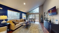 This single-story home in Concord, California offers a thoughtfully designed open-concept layout anchored by rich hardwood flooring that flows seamlessly throughout the living spaces. The living room immediately draws the eye with its striking vaulted ceiling and a bold navy blue accent wall that adds depth and sophistication to the room. Large floor-to-ceiling windows and a sliding glass door bathe the space in natural light while framing picturesque views of the surrounding mature trees, creating a seamless connection between the interior and the outdoors. A private balcony is accessible directly from the living and dining area, ideal for enjoying the natural surroundings. The open dining area comfortably accommodates a bistro-style table and chairs, positioned to take full advantage of the expansive windows. The modern kitchen features sleek dark cabinetry, crisp white quartz countertops, a classic subway tile backsplash, and stainless steel appliances. A pass-through counter connects the kitchen to the main living area, enhancing the open flow. An elegant arched doorway serves as a distinctive architectural detail, adding character as it transitions between spaces. The overall ambiance is warm, contemporary, and inviting, making this home a comfortable and stylish retreat.