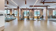 Located at 650 Wellington in Montréal's vibrant Griffintown neighbourhood, this well-appointed fitness facility spans a generously sized single floor designed to accommodate a comprehensive range of workout needs. The exercise room is thoughtfully organized into distinct training zones, each with its own flooring suited to the activities performed within it — from cushioned interlocking tiles in the functional and cardio areas to durable rubber matting in the strength and cable zones.

The cardio section features a row of treadmills positioned along large, black-framed windows that flood the space with natural light and offer street-level views of the surrounding urban landscape. Nearby, elliptical trainers and stationary bikes provide additional cardiovascular options. A dedicated free weights area houses an extensive rack of dumbbells alongside benches and medicine balls, with full-length mirrors reinforcing both form and the sense of spaciousness.

The strength training zone is anchored by a multi-functional cable machine and additional resistance equipment. A separate functional training area includes a heavy punching bag and a ballet barre set against warm wood-panelled walls. Throughout the facility, linear LED lighting and recessed pot lights create a bright, motivating ambiance, while exposed ductwork and structural elements lend an industrial aesthetic that complements the building's character.