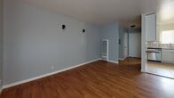 This 770-square-foot, single-story apartment at 1400 Yuba Ave, Unit 4 in San Pablo, CA offers a practical and well-appointed 2-bedroom, 1-bathroom layout. The living room features warm hardwood flooring, soft blue-gray walls, wall-mounted light fixtures, a built-in heating unit, and a sliding glass door that invites natural light and provides outdoor access. An adjacent dining area includes a pendant light fixture and continues the warm wood flooring. The kitchen is efficiently designed with white cabinetry, dark countertops, tile flooring, a window above the sink, and stainless steel appliances including a dishwasher and oven, complemented by a full-size refrigerator. The primary bedroom measures 180 square feet and features light gray luxury vinyl plank flooring, neutral gray walls, and a built-in closet with shelving and hanging rods. The second bedroom offers similar LVP flooring, a window with natural views, and a clean, neutral palette. A connecting hallway links the rooms. The bathroom is finished with wood-look LVP flooring, a white vanity, toilet, and a shower-tub combo with glass sliding doors and a window for natural ventilation. Throughout the unit, white baseboards and consistent neutral tones create a cohesive, move-in-ready atmosphere.