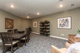 Located in Conyers, GA, this single-floor space offers a thoughtfully designed interior that balances comfort and functionality. The flooring throughout features soft, patterned carpet in muted gray tones, contributing to a calm and welcoming atmosphere.

The dining area serves as a central gathering point, anchored by a substantial dark wood dining table surrounded by matching chairs. A decorative bowl with greenery sits atop the table as a centerpiece. The walls are finished in a warm sage gray, accented by a pair of striking geometric wood art panels featuring a symmetrical chevron pattern — a standout design element that adds texture and visual interest to the space.

Adjacent to the dining area is a comfortable lounge zone, furnished with plush caramel leather armchairs and accented by a multi-tiered open shelving unit displaying books, plants, and decorative objects. Framed artwork and indoor plants further enliven the space. Recessed lighting throughout provides consistent, even illumination.

A secondary seating nook near the interior glass partition features an additional armchair, a round side table, and a decorative wall clock, creating an inviting waiting or relaxation area. The glass partition offers views into a connected corridor, enhancing the sense of openness. Overall, the space presents a polished, community-oriented environment with cohesive décor and a relaxed, functional layout.