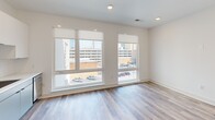 Located at 1101 Lady St in downtown Columbia, South Carolina, this single-floor unit offers a thoughtfully designed layout that maximizes its compact footprint. The open living area features light-toned hardwood-style flooring, recessed lighting, and a ceiling fan, creating a bright and functional atmosphere. Large windows along one wall frame urban views of the surrounding cityscape, filling the space with abundant natural light.

The kitchen is designed with a clean, modern aesthetic, featuring a two-tone cabinet scheme — white upper cabinets paired with soft gray lower cabinets — complemented by a white subway tile backsplash and light countertops. Stainless steel appliances, including a refrigerator, range, microwave, and dishwasher, provide full functionality, while matte black hardware adds a contemporary accent. A single-basin sink with a sleek black faucet completes the space.

The bathroom showcases large-format marble-look porcelain tile on both the floor and the tub surround, lending a clean, upscale feel. Matte black fixtures throughout the bathroom coordinate with the kitchen hardware, maintaining a cohesive design language. An additional room with vaulted ceiling detailing and wood-look flooring offers flexible use as a bedroom or workspace.