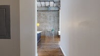 Located in the heart of downtown Houston, this two-bedroom, two-floor loft showcases a striking industrial aesthetic defined by exposed concrete walls, visible ductwork, and structural beams overhead. Rich hardwood flooring runs throughout the expansive main level, where an open-concept layout seamlessly connects the living, dining, and kitchen areas. Floor-to-ceiling windows flood the living room with natural light while framing impressive panoramic views of the Houston skyline. The kitchen is well-appointed with dark espresso cabinetry, light countertops, stainless steel appliances, and a dedicated pantry for ample storage. The generously sized primary bedroom features plush carpeting, exposed industrial ceiling details, and direct access to city views, complemented by a spacious walk-in closet with built-in shelving. The bathroom is elegantly finished with a large walk-in glass-enclosed shower clad in classic white subway tile and dark mosaic flooring. A staircase leads to the upper level, where the second bedroom offers a loft-style retreat with carpeted flooring and exposed structural ceilings. Additional functional spaces include a laundry room, utility room, and hallway. This loft delivers a distinctive blend of raw industrial character and modern residential comfort in a prime urban location.