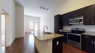 This single-floor unit offers a thoughtfully designed layout that balances modern finishes with functional living spaces. The kitchen is a standout feature, showcasing rich dark cabinetry extending to the ceiling, light granite countertops, a classic white subway tile backsplash, and a full suite of stainless steel appliances including a range, over-the-range microwave, and refrigerator. A central island with an undermount sink and matching granite surface provides additional prep space and opens directly to the living area, creating a seamless flow ideal for everyday living and entertaining. Track lighting overhead enhances the kitchen's polished aesthetic.

The living area is bathed in natural light from large windows and a glass door, highlighting the rich, dark hardwood flooring and soaring ceiling height that lends an open, airy feel to the space. The bedrooms offer a comfortable contrast with soft carpeting and generous natural light streaming through tall windows with blinds, creating a calm and restful atmosphere.

The bathroom is well-finished with tile flooring, a tub and shower combination with tile surround, a dark vanity with granite countertop, an undermount sink, and a large mirror. Clean, neutral tones throughout tie the space together, making it a cohesive and move-in-ready home.