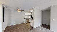 This single-floor unit offers a clean, functional layout designed for comfortable everyday living. The open-concept main area seamlessly connects the living space and kitchen, with durable wood-look vinyl plank flooring running throughout the kitchen and dining zones, while plush carpeting defines the living and bedroom areas. A ceiling fan with integrated lighting keeps the living space well-ventilated and comfortable.

The kitchen is efficiently organized and features crisp white cabinetry, granite-look countertops, a stainless steel sink with a modern faucet, and a full suite of appliances including a stainless steel dishwasher, black refrigerator, and a freestanding range. A peninsula counter provides additional workspace and helps define the transition between the kitchen and living area.

The bedroom is generously sized with soft carpeting underfoot and a window that brings in natural light and a view of the surrounding greenery. Neutral gray walls throughout the unit create a calm, versatile backdrop well-suited to a variety of décor styles.

The bathroom is finished with clean white tilework surrounding a full soaking tub and shower combination, complete with chrome fixtures and a safety grab bar. Textured ceilings are consistent throughout the unit, adding a classic residential character to the overall interior.