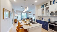 This single-floor residence showcases a cohesive, contemporary design built around a striking navy and white color palette. The open-concept kitchen serves as the centerpiece, featuring bold navy lower cabinetry paired with crisp white upper cabinets, a white subway tile backsplash, stainless steel appliances, and a spacious island with quartz countertops and seating for casual dining. Pendant lighting above the island adds a polished finishing touch.

The living area flows naturally from the kitchen and is anchored by light hardwood flooring, a ceiling fan, and a textured white brick accent wall. A glass door opens directly to an outdoor space, inviting natural light and garden views into the room.

The primary bedroom features a bold blue circular-patterned accent wall, a wood-slab headboard, and natural light from a well-dressed window. The secondary bedroom offers a quieter aesthetic with neutral carpet, blue patterned curtains, and greenery accents.

The bathroom maintains the navy design theme with navy vanity cabinetry, quartz countertops, a large mirror, and a tiled walk-in shower. Throughout the residence, consistent use of navy, white, and warm wood tones creates a stylish and well-coordinated living environment.