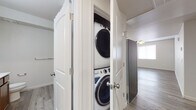 This single-floor residence offers a thoughtfully designed layout with a cohesive neutral palette throughout. The kitchen serves as a functional centerpiece, featuring rich wood cabinetry, light stone-finish countertops, stainless steel appliances including a French door refrigerator, electric range, over-the-range microwave, and dishwasher. A peninsula provides additional counter space and connects the kitchen to the adjacent dining or living area, which features wood-look flooring and a ceiling fan with lighting.

The bedrooms are carpeted for comfort and each includes a reach-in closet with a hanging rod. Ceiling fans are present in the main living spaces, and windows allow natural light to filter in throughout. A dedicated laundry closet houses a stacked washer and dryer unit behind bifold doors, offering in-unit convenience.

Two bathrooms serve the residence. One features a single-basin vanity with a dark wood cabinet and framed mirror, alongside a tub-shower combo and wood-look flooring. The second bathroom presents an extended white stone countertop vanity, warm wood cabinetry, a large wall mirror, and wood-look flooring. The overall ambiance is clean, functional, and move-in ready.