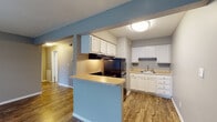 Located at 5028 Dierker Rd in Columbus, Ohio, this single-floor unit offers a practical and well-organized layout suited for comfortable everyday living. The entryway greets residents with warm wood-look vinyl flooring and flanking louvered closet doors, providing generous storage from the moment you step inside. The open-concept living and dining area is defined by cool blue-gray accent walls and continuous wood-look flooring, creating a cohesive, modern aesthetic. A peninsula with a light countertop separates the living space from the kitchen, offering a convenient breakfast bar setup. The kitchen is well-equipped with crisp white cabinetry extending to the upper walls, black appliances including a gas range and refrigerator, a double sink, and light-toned countertops — all set atop matching wood-look flooring. The bedroom features plush wall-to-wall carpeting, neutral gray walls, and a window that allows natural light to fill the room, along with a spacious walk-in closet with built-in hanging rods and shelving. The bathroom includes a tub-shower combination, a white vanity with a light countertop, wood-look flooring, and clean, neutral finishes throughout. The overall ambiance is clean, updated, and move-in ready.