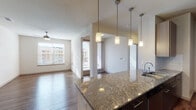 Located at 201 E Eldorado Pkwy in Little Elm, Texas, this thoughtfully designed single-floor unit offers a seamless open-concept layout that connects the kitchen, dining, and living areas. The kitchen is a standout feature, boasting richly veined granite countertops, two-tone dark and light cabinetry, a classic subway tile backsplash, and a full suite of stainless steel appliances including an electric range with over-the-range microwave and a full-size refrigerator. A large granite-topped island with an undermount sink and stylish pendant lighting serves as both a functional workspace and a natural focal point. Built-in open shelving adjacent to the kitchen adds practical display and storage options. The expansive living area is bathed in natural light from multiple windows and features warm hardwood-style flooring and a ceiling fan throughout. The bathroom continues the home's design language with granite vanity countertops, tile-surround bathtub, and dark wood cabinetry, complemented by a walk-in closet with wire shelving for generous storage. The overall ambiance is clean, contemporary, and bright, offering a well-appointed living experience in the heart of Little Elm.