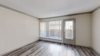 This single-floor unit offers a well-organized layout that balances comfortable living and functional design. The living area is bright and inviting, featuring wood-look laminate flooring in a neutral gray tone, crown molding, and a large picture window fitted with vertical blinds that fill the space with natural light. A secondary door provides direct access to the exterior, enhancing the open, airy feel of the room.

The open floor plan connects the living area to the rest of the unit, with a pass-through window offering a view into the kitchen. The galley-style kitchen is well-equipped with warm wood cabinetry, granite-style countertops, and black appliances including a range, refrigerator, and dishwasher. Matching wood-look flooring continues throughout the kitchen and hallway areas.

The bedrooms are carpeted for added comfort and feature textured walls, natural light from windows with blinds, and ceiling fans for year-round climate control. Closet access is conveniently integrated into each bedroom. A vanity area with matching cabinetry and granite-style countertops connects to the bathroom corridor, maintaining a consistent design aesthetic throughout the unit. The overall palette of soft neutrals and warm wood tones creates a clean, cohesive living environment.