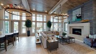 This single-story clubhouse in Panama City Beach, Florida, offers a sophisticated coastal gathering space defined by elegant architectural details and a warm, welcoming ambiance. The entrance greets visitors with soaring double-height ceilings, floor-to-ceiling windows, and light-toned tile flooring that flows seamlessly throughout the space. A grand reception area with a central table serves as the welcoming hub, adorned with decorative botanicals and community literature.

The main lounge is a showpiece, featuring dramatic wood-plank ceilings with exposed beams, large candle-style chandelier fixtures, and an expansive wall of windows that floods the room with natural light and offers views of the outdoor pool area. A contemporary fireplace with a floor-to-ceiling tile surround anchors one end of the lounge, complemented by plush sectional seating and layered area rugs.

Adjacent to the lounge is a well-appointed kitchen area showcasing a striking marble-topped island with bar seating, a decorative mosaic tile backsplash, and custom cabinetry. A separate lounge nook, finished in soft coastal blue tones with wood-ceiling accents, features curated bird artwork and intimate seating arrangements, ideal for private conversations or community gatherings. Every detail of this clubhouse reflects a refined coastal design aesthetic.